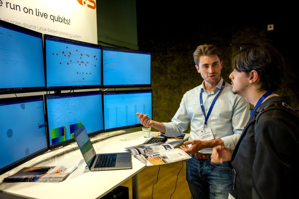 OrangeQS team in front of the new 6 screen console, also on display at the APS March Meeting 2026 in Denver.